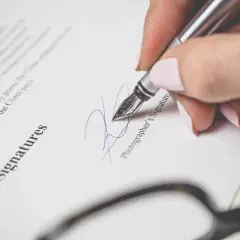 Mano con pluma estilográfica firma un documento. La firma se realiza encima o debajo del nombre "Photographer's Signature".
